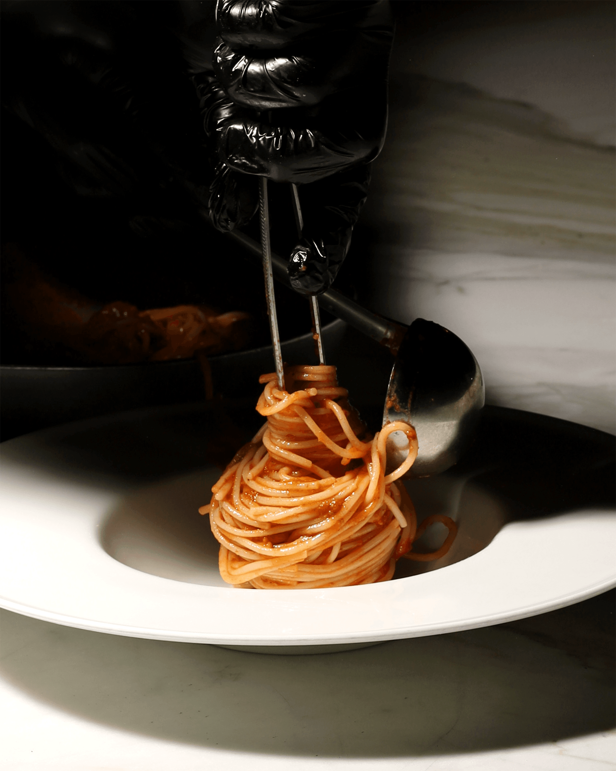 Chef twirling a fresh tomato pasta onto a plate with tongs